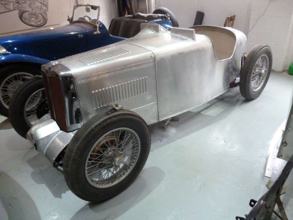 The new aluminium body sitting on the MG TA chassis in a workshop, still in bare unpainted metal.