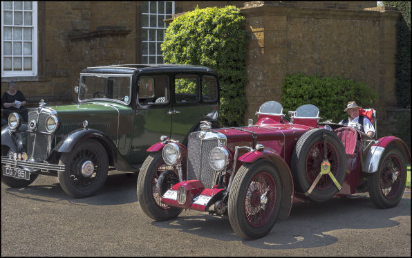 Ruby parked on gravel beside a green and black pre-war saloon in front of a stone building.