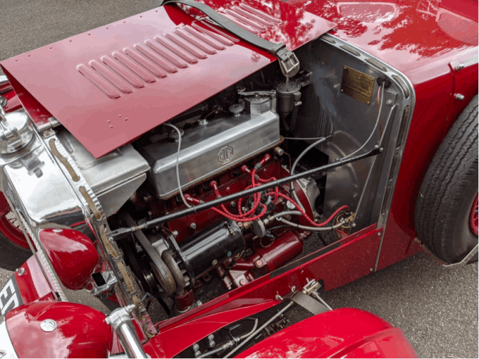 The ignition side of the engine with the bonnet panel propped open: the MG rocker cover, red HT leads running from the distributor to the plugs, and the dynamo below.