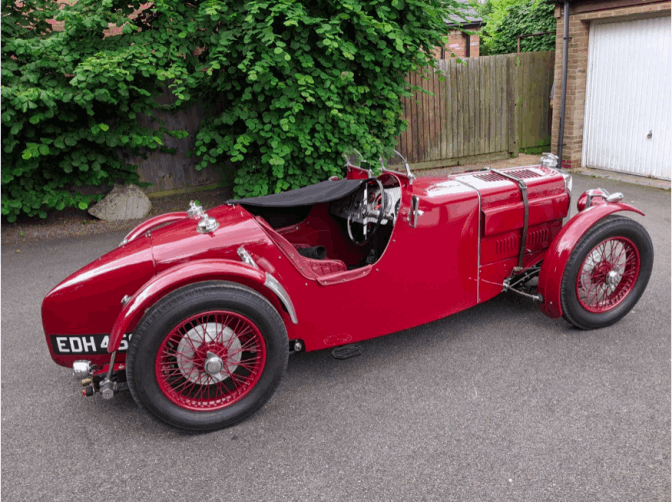 Side view of the car on a driveway, showing the full length of the body and the tapered tail.